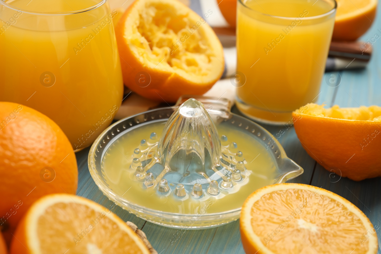 Photo of Squeezer, fresh oranges and juice on blue wooden table