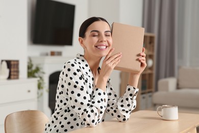 Photo of Happy young woman with parcel at table indoors. Internet shopping