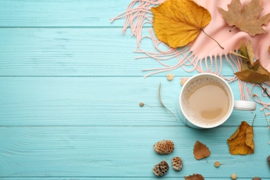 Flat lay composition with cup of hot drink and autumn leaves on light blue wooden table, space for text. Cozy atmosphere