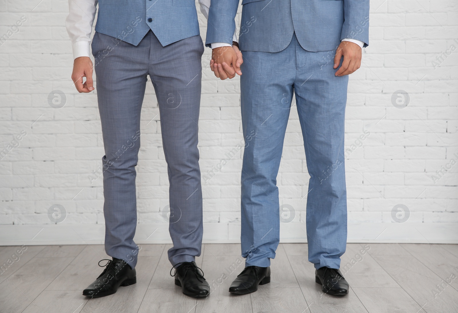 Photo of Newlywed gay couple holding hands near brick wall indoors