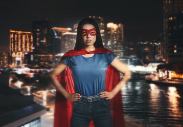 Confident young woman wearing superhero costume and beautiful cityscape in night on background