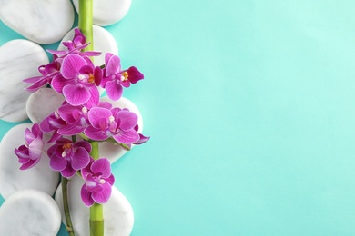 Photo of Orchid with spa stones on turquoise background, flat lay. Space for text