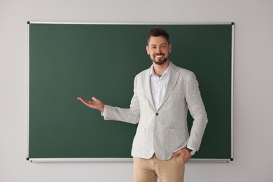 Photo of Happy teacher explaining something at blackboard in classroom. Space for text