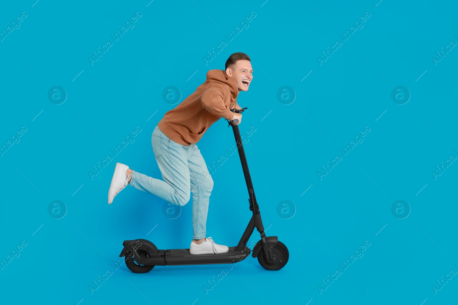 Photo of Emotional man riding modern electric kick scooter on light blue background