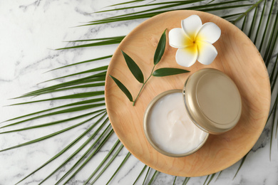 Composition with cosmetic product and tropical flower on white marble table, top view