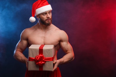 Attractive young man with muscular body holding Christmas gift box on color background, space for text