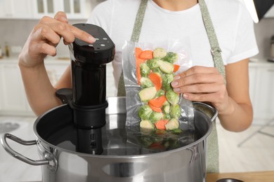 Woman putting vacuum packed vegetables into pot and using thermal immersion circulator, closeup. Sous vide cooking