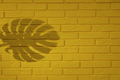 Shadow of monstera leaf on yellow brick wall, space for text