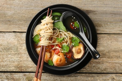 Photo of Delicious ramen with chopsticks and spoon in bowl on wooden table, top view. Noodle soup