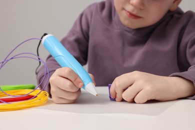 Boy drawing with stylish 3D pen at white table, closeup