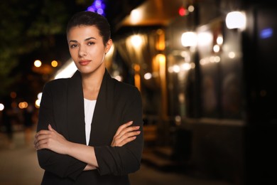 Portrait of hostess in uniform and blurred view of cafe with outdoor terrace at night. Space for text