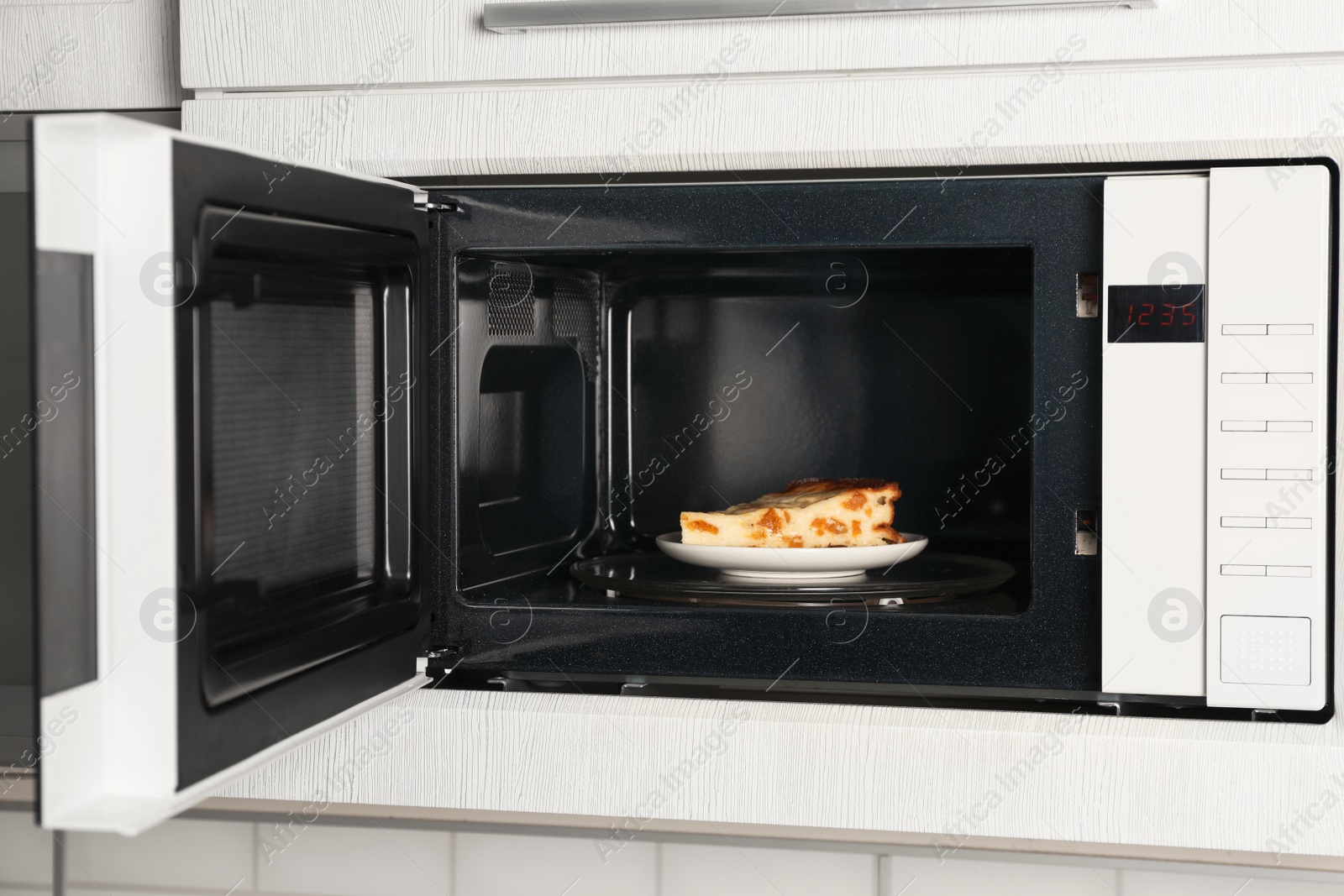 Photo of Open modern microwave oven with dessert in kitchen