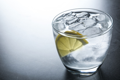 Photo of Water with ice cubes and lemon on grey table, closeup. Space for text