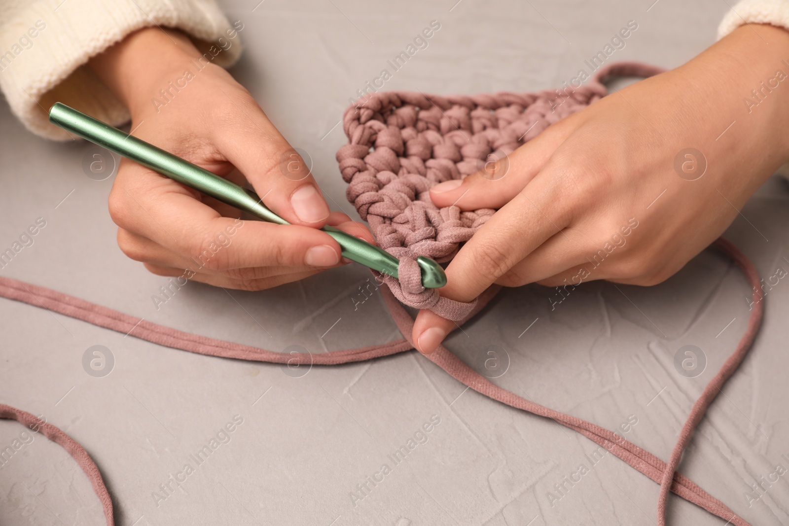 Photo of Woman crocheting with threads at grey table, closeup. Engaging hobby
