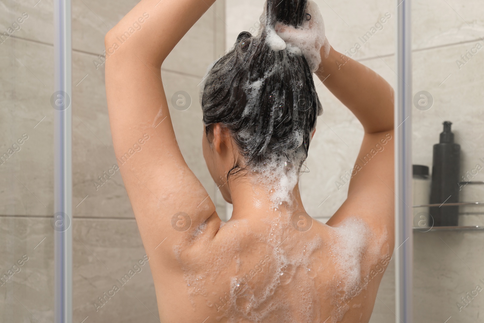 Photo of Woman washing hair in shower stall, back view