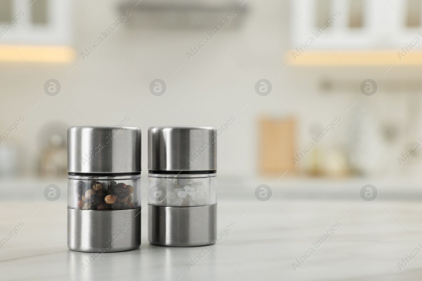 Photo of Salt and pepper mills on white marble table in kitchen. Space for text