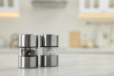 Salt and pepper mills on white marble table in kitchen. Space for text