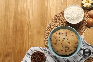 Photo of Bowl with dough and ingredients for cooking chocolate chip cookies on wooden table, flat lay. Space for text