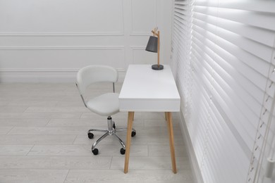 Photo of Stylish workplace with white desk and comfortable chair near window indoors. Interior design