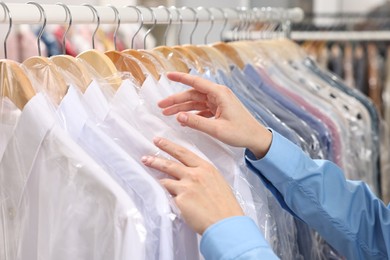 Dry-cleaning service. Woman taking shirt in plastic bag from rack indoors, closeup