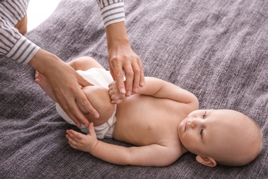 Young woman massaging cute little baby on blanket