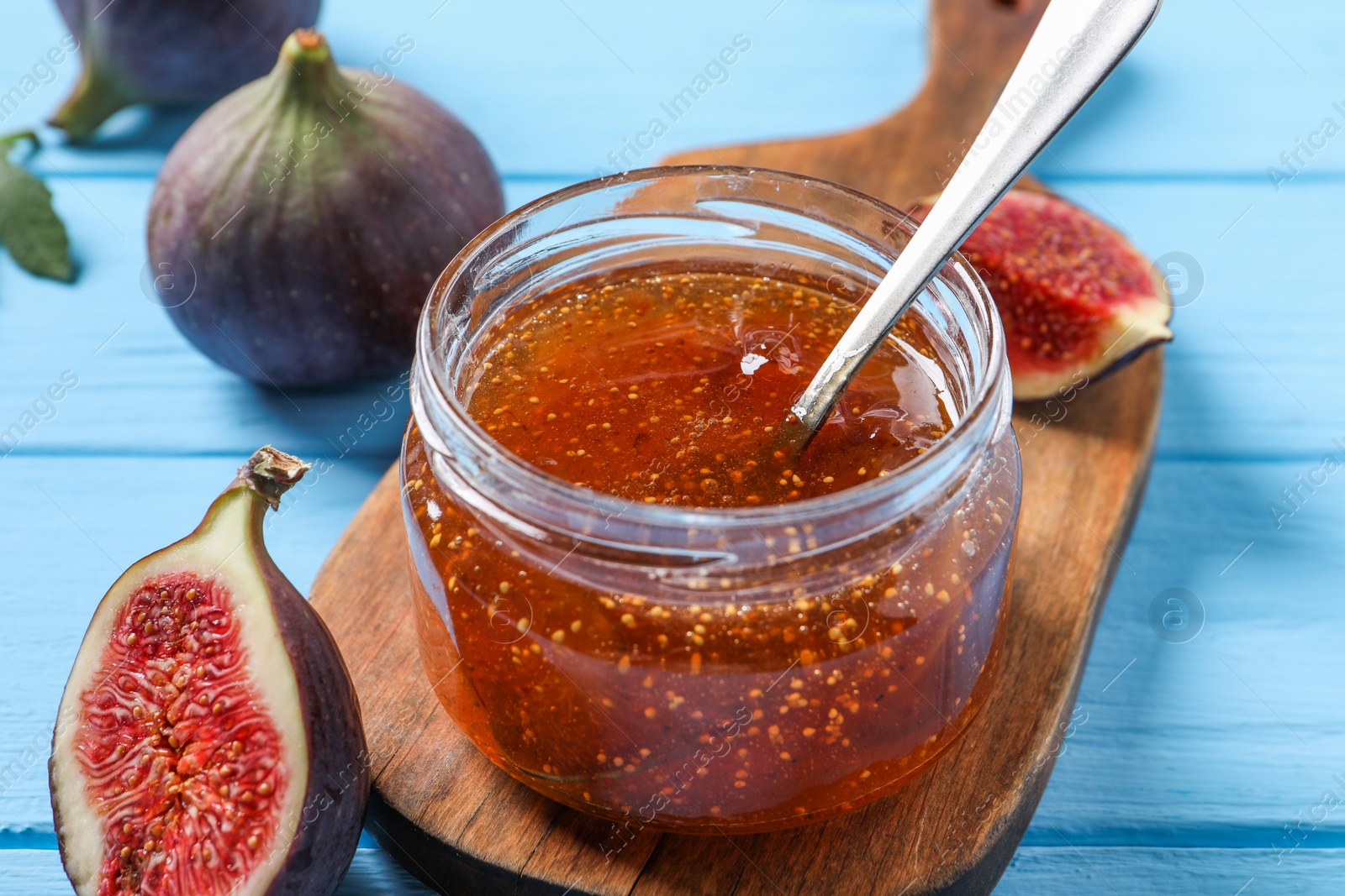 Photo of Jar of tasty sweet jam and fresh figs on light blue wooden table, closeup