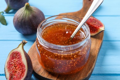 Jar of tasty sweet jam and fresh figs on light blue wooden table, closeup