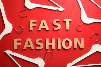 Photo of Phrase FAST FASHION made of wooden letters and white hangers on red background, flat lay