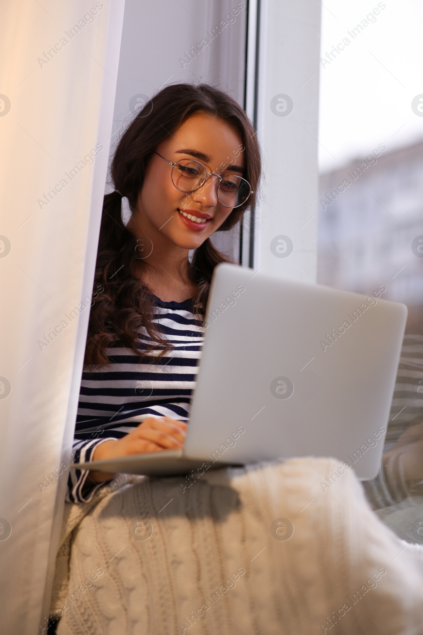 Photo of Young woman using laptop near window at home. Winter atmosphere