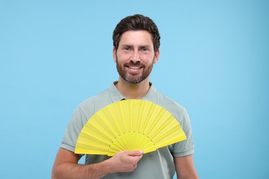Photo of Happy man holding hand fan on light blue background
