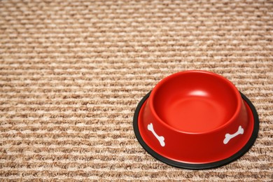 Photo of Empty red feeding bowl on soft carpet. Space for text