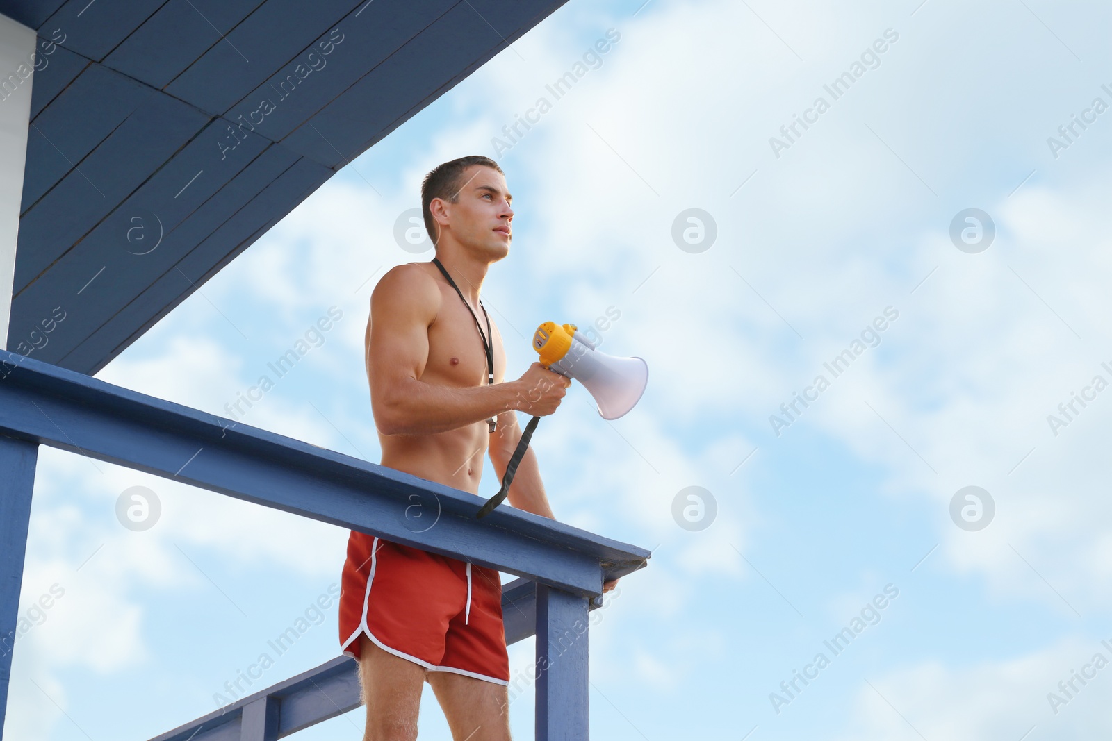 Photo of Handsome lifeguard with megaphone on watch tower against sky