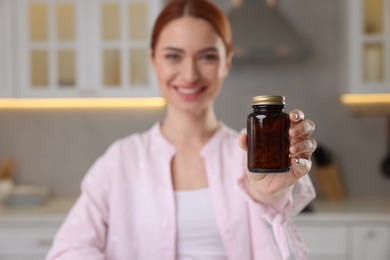 Beautiful young woman with jar of vitamin pills at home, selective focus