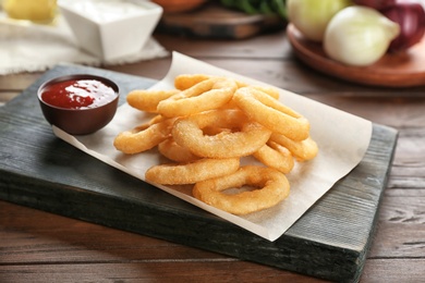 Photo of Tasty fried onion rings and bowl of ketchup on wooden table