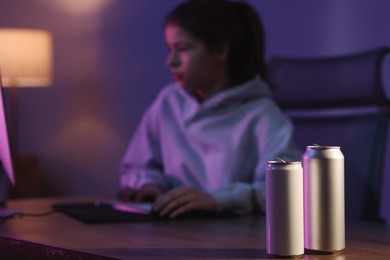 Photo of Girl playing computer game at home, focus on cans with energy drink