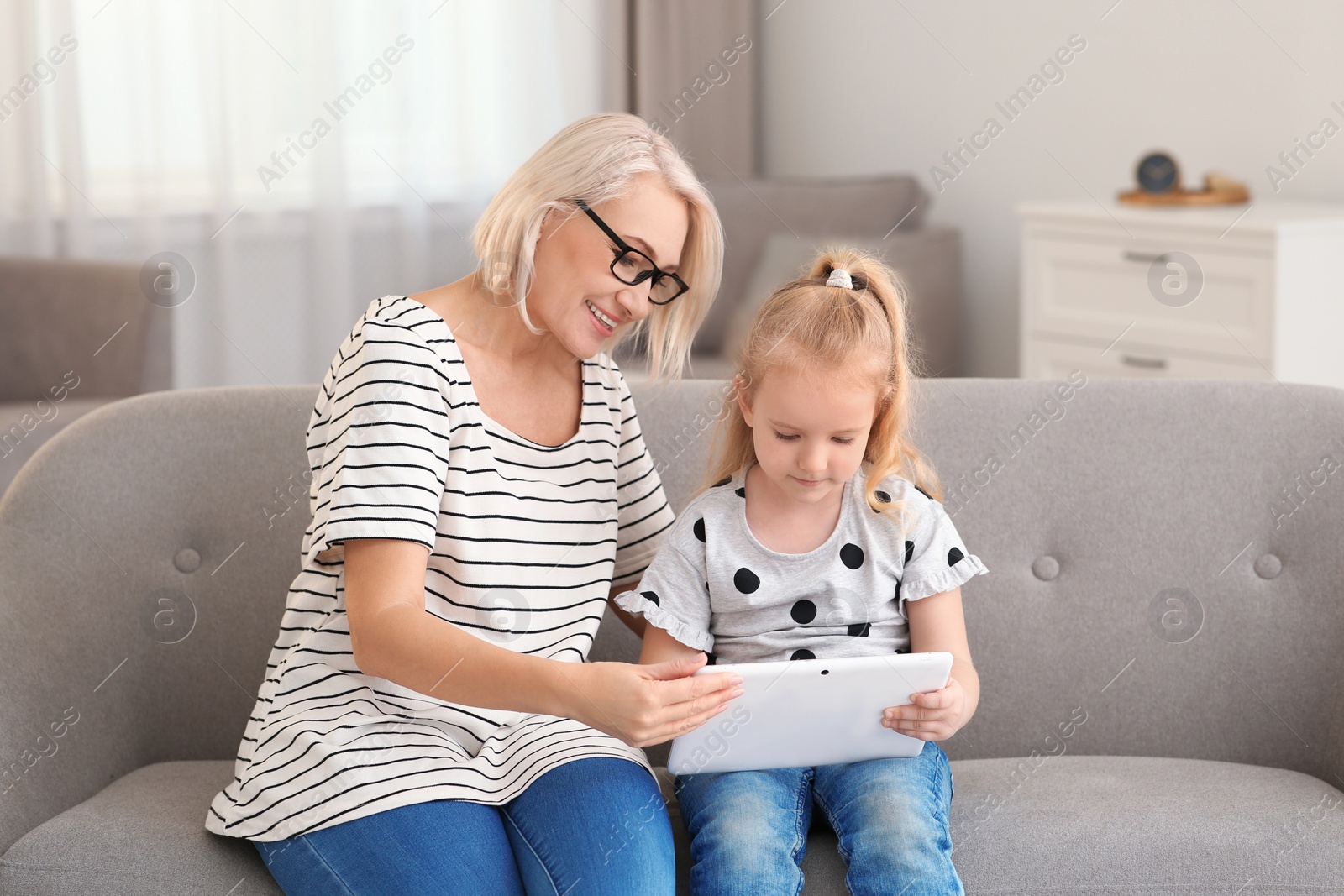 Photo of Portrait of mature woman and her granddaughter using tablet together in living room