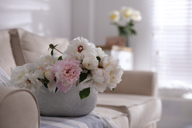 Photo of Bouquet of beautiful peony flowers in basket on sofa. Space for text