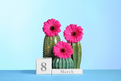 Photo of Composition with decorative cacti and flowers on table against color background. International Women's Day