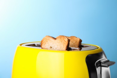 Photo of Yellow toaster with roasted bread against light blue background, closeup
