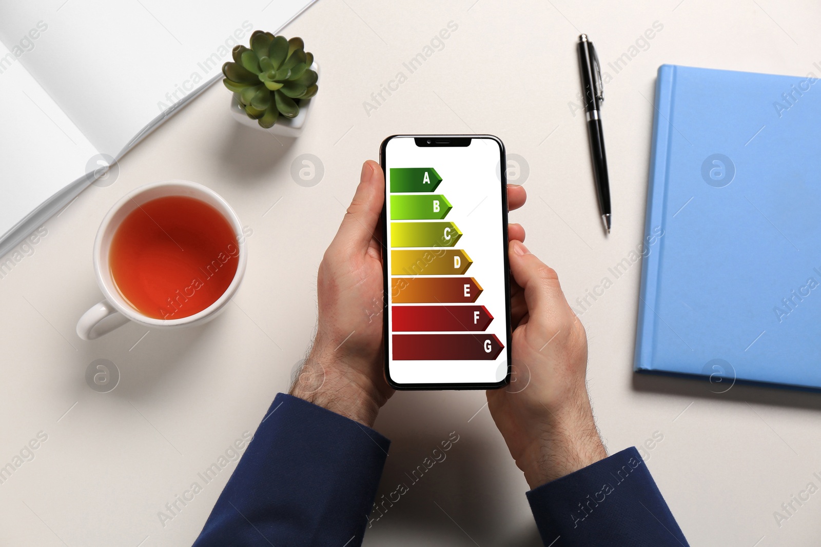 Image of Energy efficiency. Man using smartphone with colorful rating on display at white table, top view