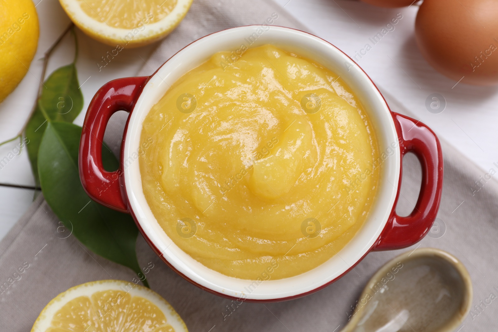 Photo of Delicious lemon curd in bowl, ingredients and spoon on table, flat lay