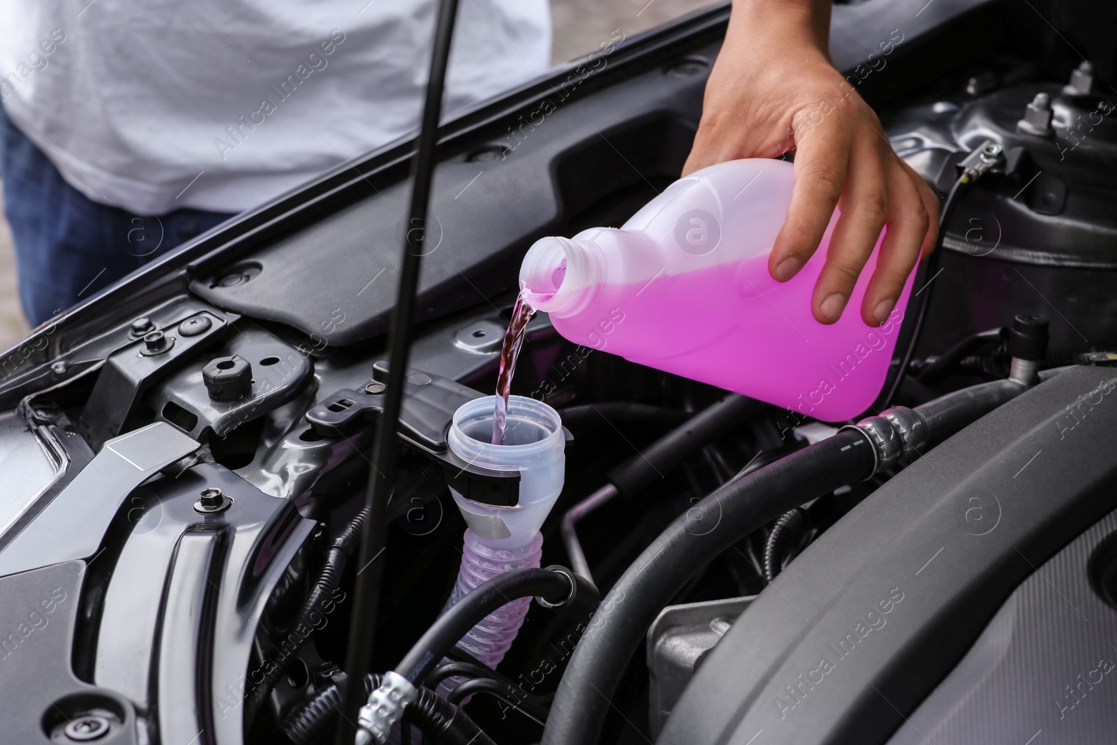 Photo of Man pouring liquid from plastic canister into car washer fluid reservoir, closeup