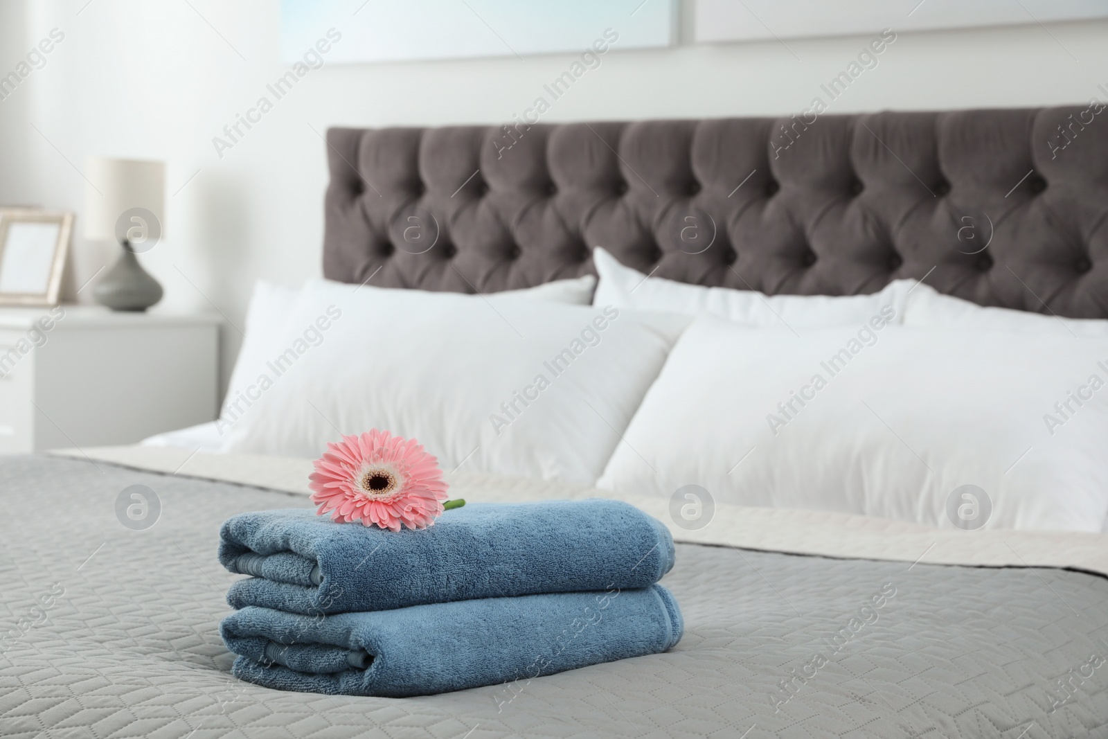 Photo of Stack of clean towels with flower on bed indoors. Space for text