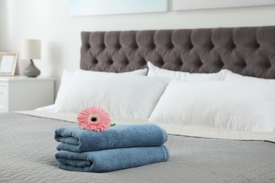 Stack of clean towels with flower on bed indoors. Space for text