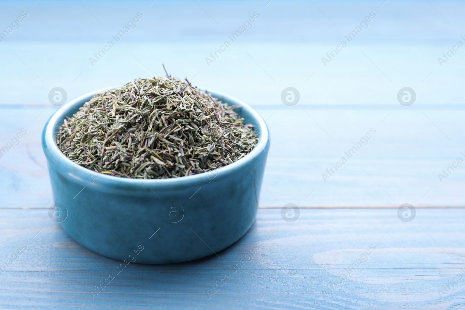 Photo of Ceramic bowl with dried thyme on light blue wooden table, closeup. Space for text
