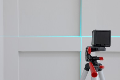 Cross line laser level on tripod in front of light wall