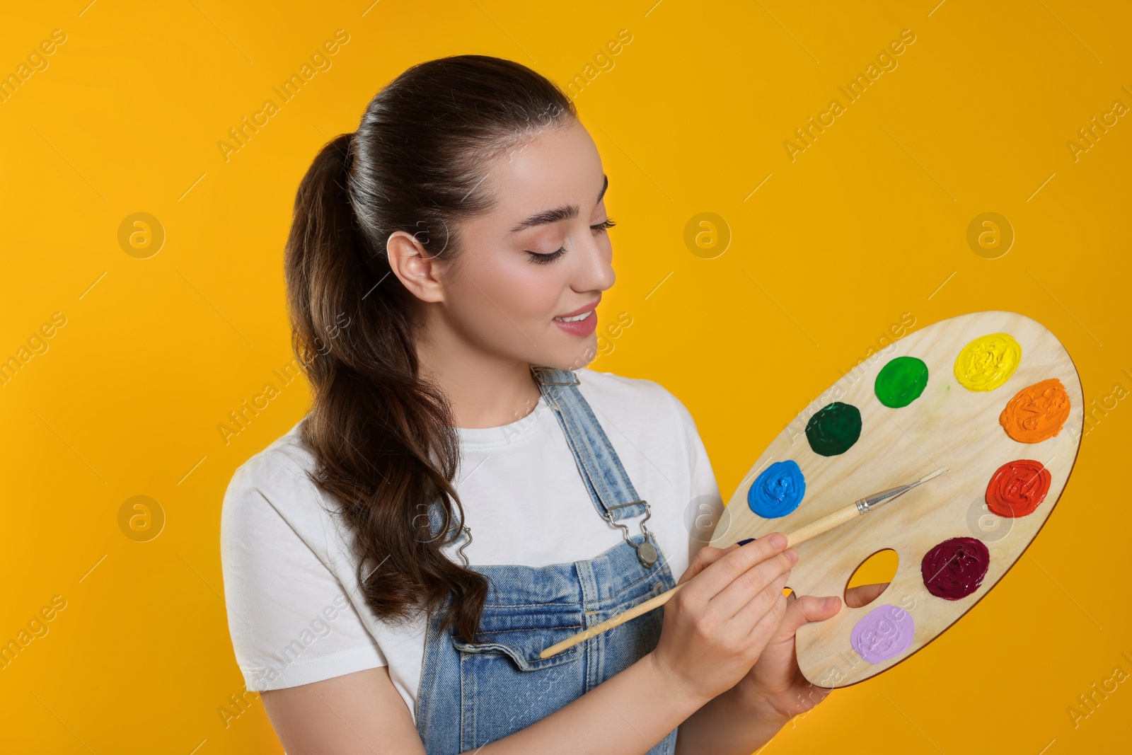 Photo of Woman with painting tools on yellow background. Young artist