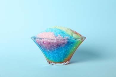 Rainbow shaving ice in glass dessert bowl on light blue background