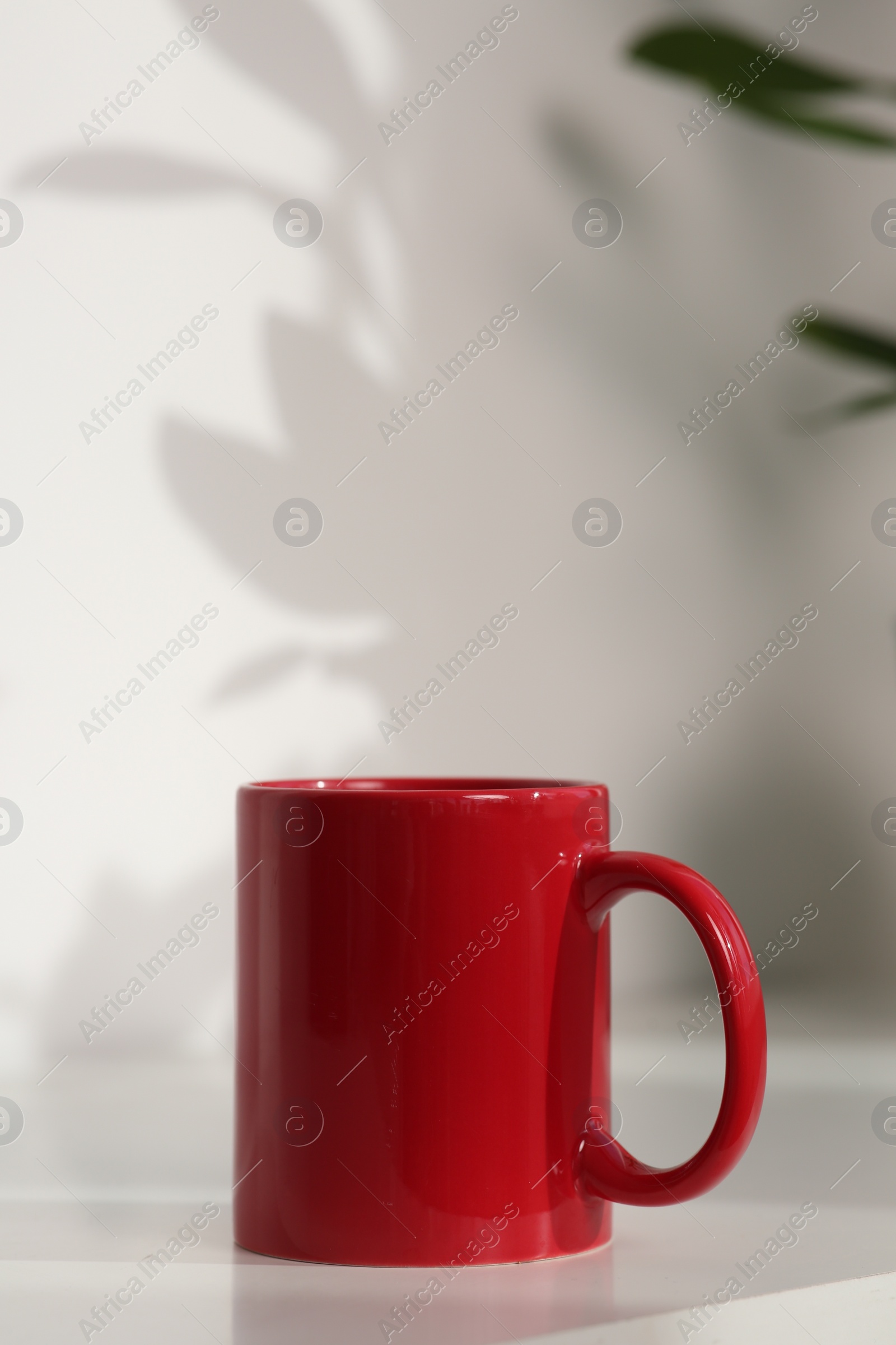 Photo of Red ceramic mug on white table indoors. Mockup for design