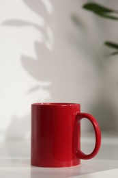 Red ceramic mug on white table indoors. Mockup for design